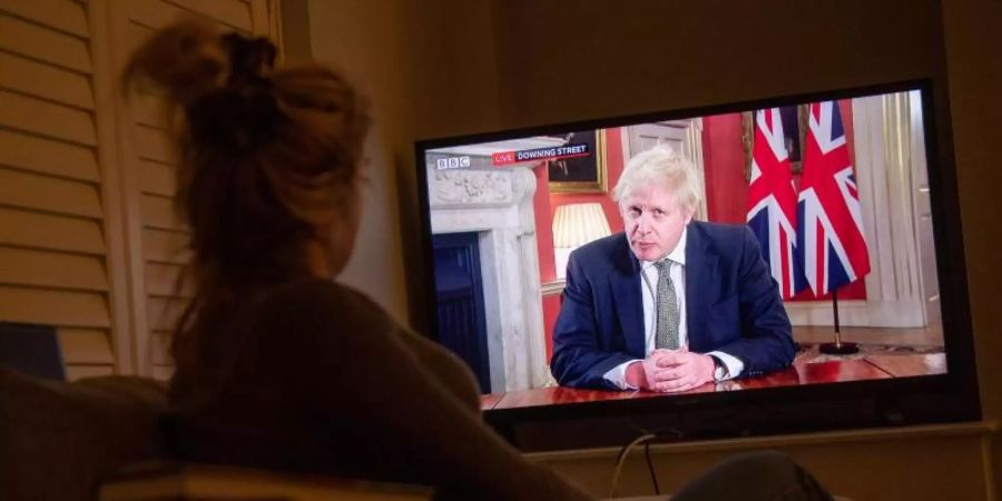 Eine Frau verfolgt im Fernsehen die Ansprache von Premierminister Boris Johnson an die Nation. Foto: Jacob King/PA Wire/dpa