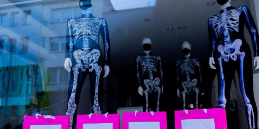 Schaufensterfiguren, die Anzüge mit Skelettmotiv und Mund-Nasen-Schutz tragen, stehen in einem geschlossenen Geschäft in der Innenstadt von Köln. Foto: Rolf Vennenbernd/dpa