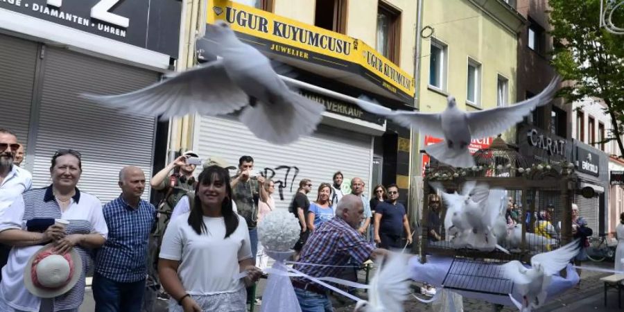 Teilnehmer einer Schweigeminute lassen auf der Kölner Keupstrasse am 15. Jahrestag zur Erinnerung an den NSU-Nagelbombenanschlag, bei dem dort 22 Menschen verletzt wurden, 15 weisse Tauben aufsteigen. Foto: Roberto Pfeil