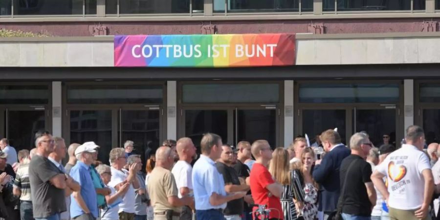 Teilnehmer des Wahlkampfauftakts der AfD-Jugendorganisation Junge Alternative stehen vor einem Transparent an der Stadthalle mit der Aufschrift «Cottbus ist bunt». Foto: Patrick Pleul