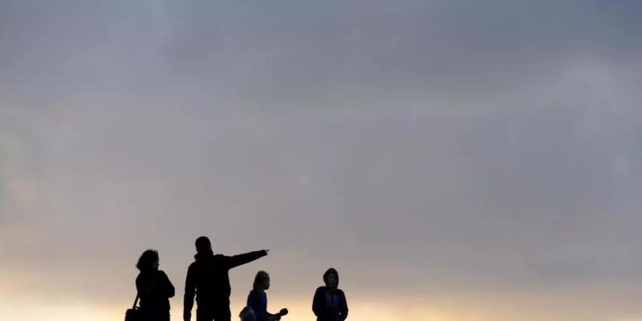 Eine Familie beim Spaziergang unterm abendlichen Wolkenhimmel. Foto: picture alliance / dpa