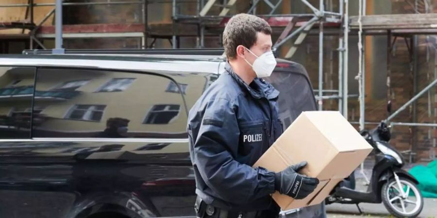 Ein Polizist trägt sichergestelltes Beweismaterial zu einem Auto. Foto: Paul Zinken/dpa-Zentralbild/dpa