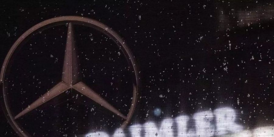 Das Logo der Daimler-AG ist an der Konzernzentrale zu sehen, im Vordergrund ist ein Mercedes-Stern auf einer Flagge abgebildet, die voller Regentropfen ist. Foto: Marijan Murat/dpa