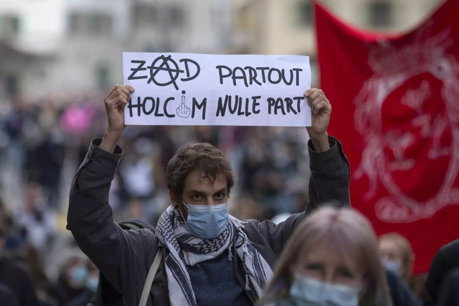 Ein Demonstrant in Lausanne hält ein Schild in die Luft, dass sich gegen Holcim richtet.