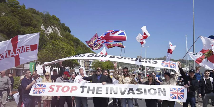 Demonstranten nehmen mit Fahnen und einem Banner mit der Aufschrift «Stop the Invasion» (Stoppt die Invasion) an einem Protest gegen Flüchtlinge, die über den Ärmelkanal nach Kent kommen, teil. Foto: Andrew Matthews/PA/AP/dpa - ACHTUNG: Nur zur redaktionellen Verwendung im Zusammenhang mit der aktuellen Berichterstattung und nur mit vollständiger Nennung des vorstehenden Credits