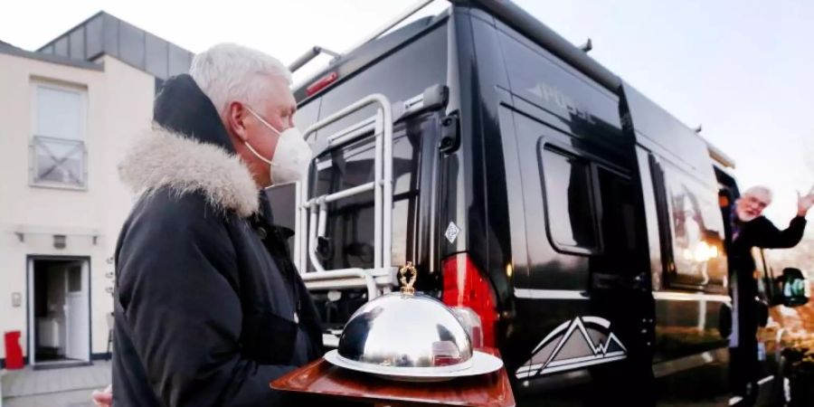 Hans-Werner Scherer (l.), Gastwirt des Restaurantes Bootshaus Ruhreck", bringt seinem Kunden Hubert eine Vorspeise zu seinem Wohnmobil. Foto: Roland Weihrauch/dpa