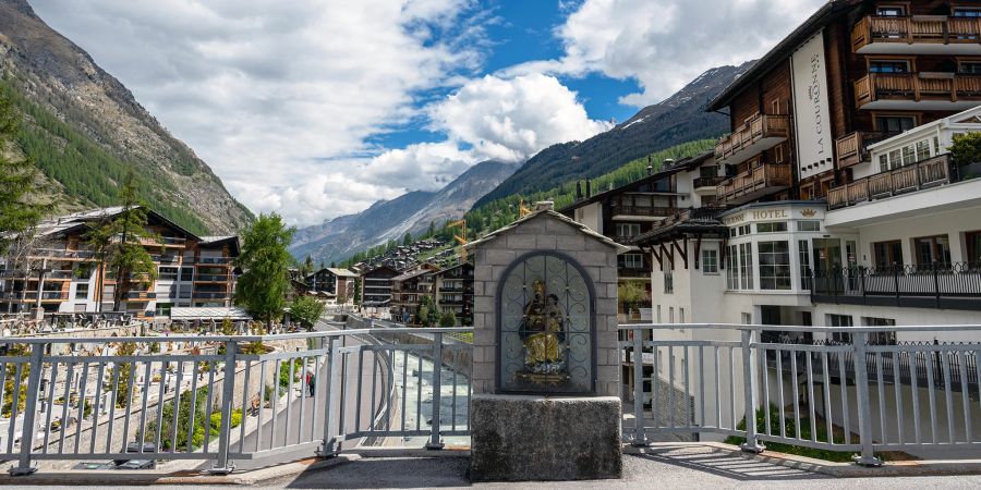 Eine Marienstatue, der Dorffriedhof, das Hotel La Couronne und die Vispa in Zermatt.