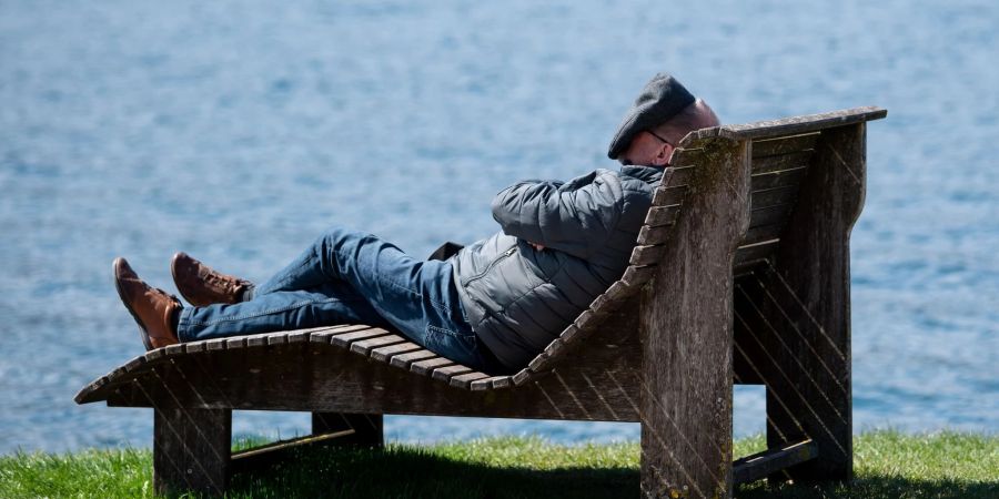 Ein Mann liegt am Ufer des Tegernsees in der Sonne und deckt sein Gesicht ab.