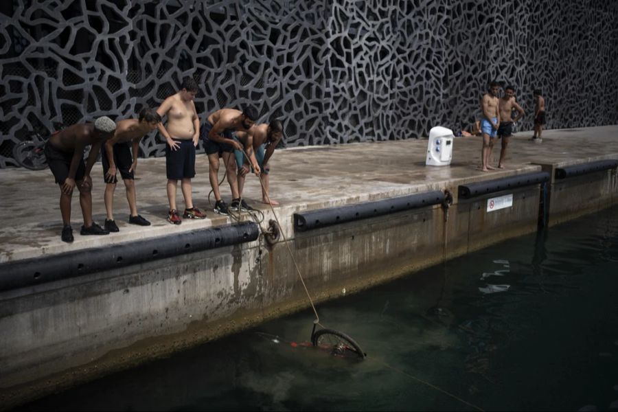 Was man so findet, wenn man an neuen Orten schwimmen geht: Junge Männer ziehen ein Fahrrad aus dem Hafen von Marseille, das sie dort bei ihrer Abkühlung gefunden haben.