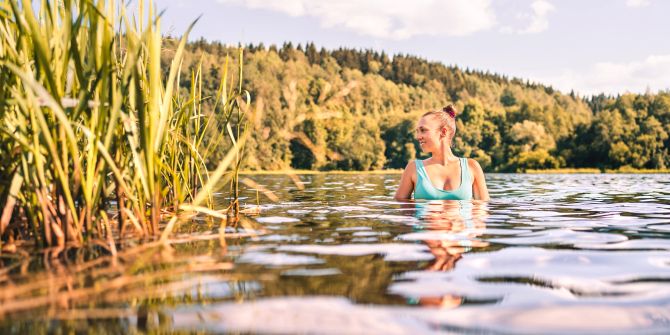 Stockfotografie See in Finnland. Glücklich lächelnde Frau, die im Sommer im Wasser schwimmt. Finnische Natur bei Sonnenuntergang.
