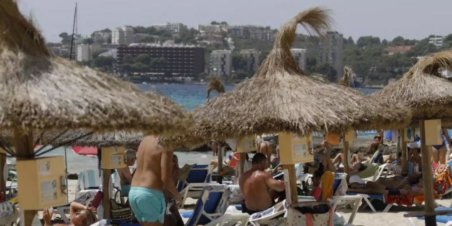 Einheimische und Touristen liegen am Strand Cala Major in Palma de Mallorca. Foto: Clara Margais/dpa