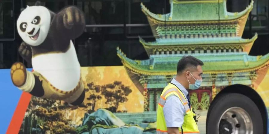 Ein Verkehrspolizist steht bei Probefahrten neben einem Bus, auf dem für den Vergnügungspark von Universal Studios geworben wird. Foto: Ng Han Guan/AP/dpa