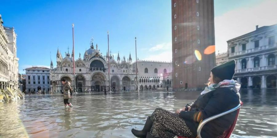 Eine Frau sitzt auf einem Stuhl im Hochwasser auf dem Markusplatz. Foto: Claudio Furlan/LaPresse via ZUMA Press/dpa