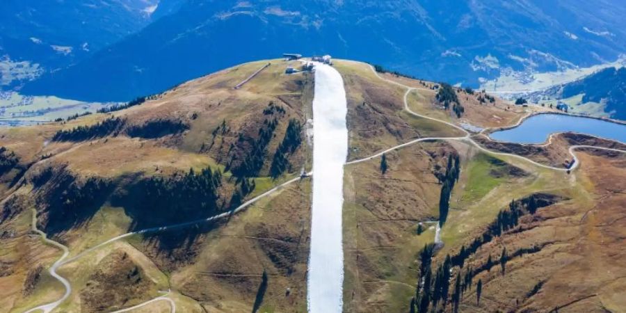 Für eine schmale Piste wurde konservierter Schnee aus dem vergangenen Winter als Band in der Berglandschaft auf der noch grünen Resterhöhe in den Kitzbüheler Alpen aufgetragen. Foto: Expa/Johann Groder/APA/dpa