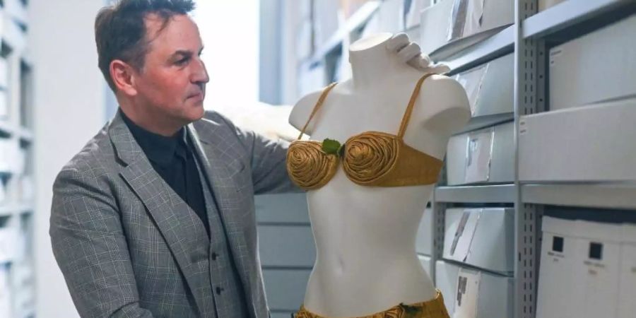 Reinhold Weinmann, Museumsdirektor des Bikini Art Museums, steht neben einem goldenen Bikini aus der Zeit um 1950 von Louis Réard. Foto: Armin Weigel/dpa