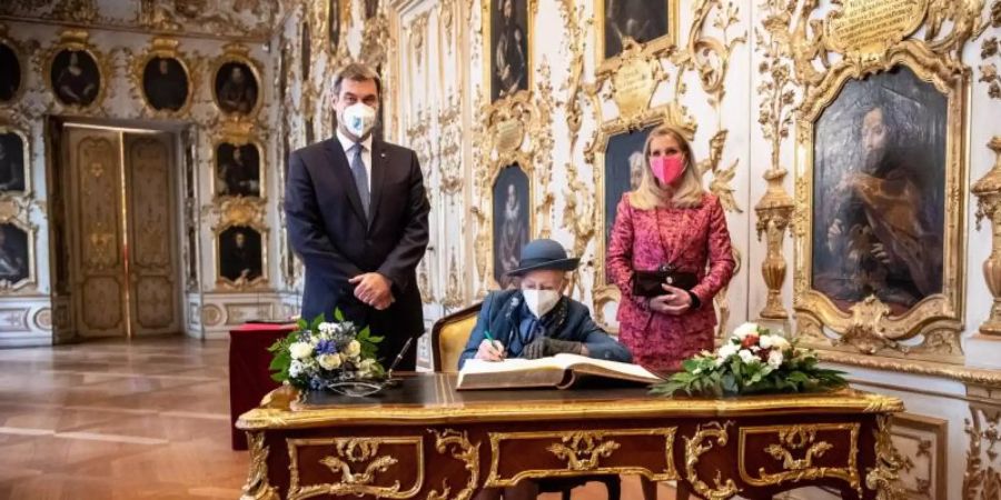 Königin Margrethe II. von Dänemark (M) trägt sich in der Residenz München in das Gästebuch der Bayerischen Staatsregierung ein. Neben ihr: neben Markus Söder (CSU), Parteivorsitzender und Ministerpräsident von Bayern, und seine Frau Karin Baumüller-Söder. Foto: Matthias Balk/dpa-Pool/dpa