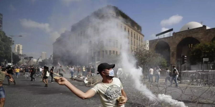 Ein Demonstrant wirft einen Stein auf Sicherheitskräfte. Foto: Hassan Ammar/AP/dpa