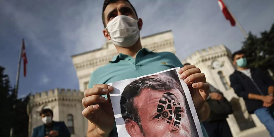 Ein junger Mann hält in Istanbul ein mit einem Schuhabdruck versehenes Foto von Emmanuel Macron in die Kamera. Foto: Emrah Gurel/AP/dpa