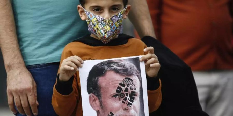 Ein Kind hält in Istanbul ein mit einem Schuhabdruck versehenes Foto von Emmanuel Macron in die Kamera. Foto: Emrah Gurel/AP/dpa