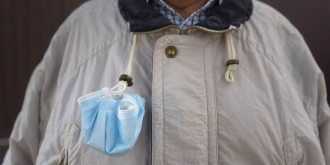 Ein Mann trägt seine Hygienemaske zum Schutz vor dem Coronavirus an seiner Jacke. Coronavirus Maske