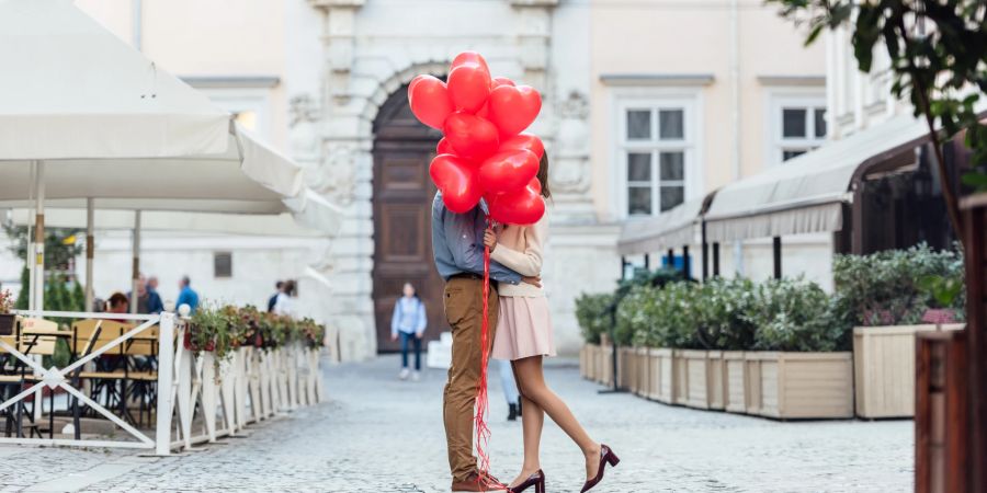 paar versteckt sich hinter herzförmigen luftballons