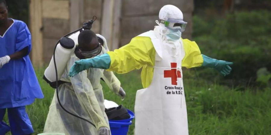 Ein Helfer des Roten Kreuzes wird nach einem Einsatz in einem Ebola-Behandlungszentrum von einem Kollegen mit Desinfektionsmittel eingesprüht. Foto: Al-Hadji Kudra Maliro/AP