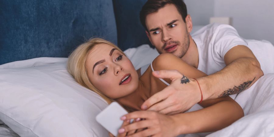 mann und frau im bett, frau mit handy des partners