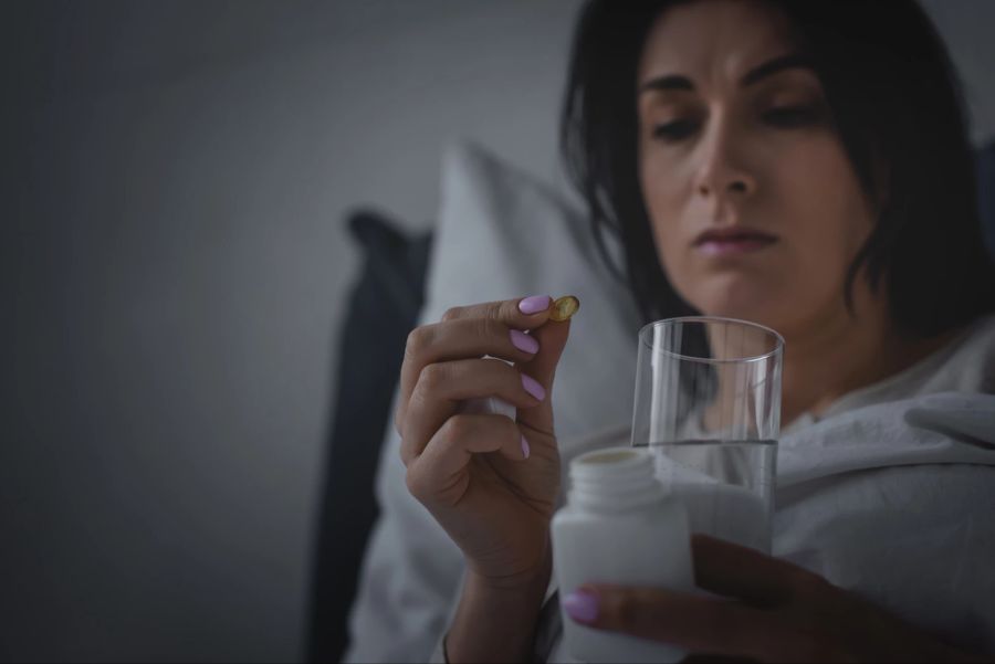 frau mit pillen in der hand, schlaflos, grauer hintergrund