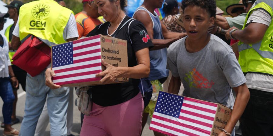 Von den Erdbeben betroffene Menschen tragen humanitäre Hilfsgüter aus den USA, nachdem sie diese erhalten haben. Foto: Ariana Cubillos/AP/dpa