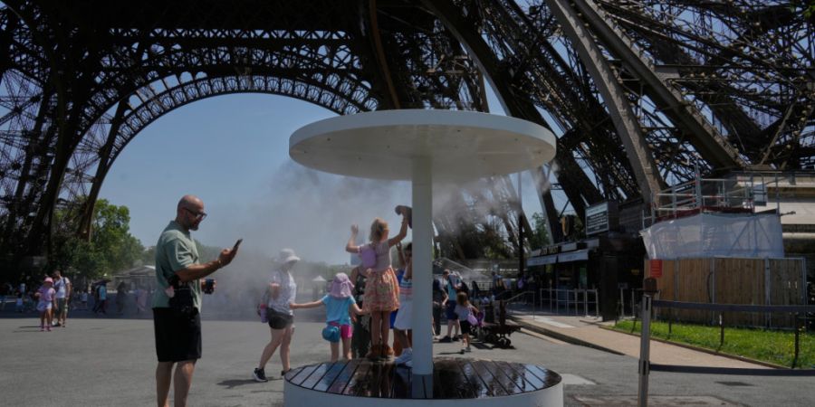 ARCHIV - Menschen erfrischen sich am Eiffelturm unter einem Wassersprühnebel. Foto: Michel Euler/AP/dpa