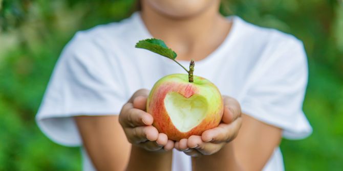 Kinderhände halten einen Apfel mit Herz