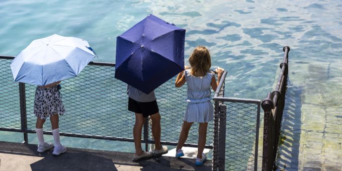 Drei Kinder schützen sich in Genf mit Schirmen vor der prallen Sonne. Wetter Kinder Genf