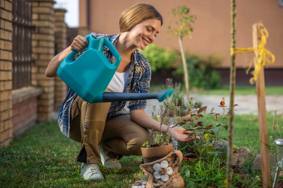 Glückliche Frau im Garten mit Giesskanne, Bewässerung, Pflanzen