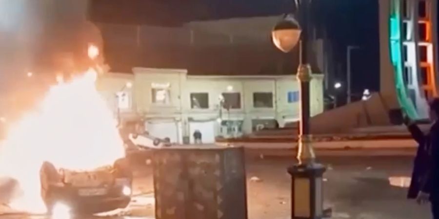 HANDOUT - Dieser Ausschnitt aus einem vom iranischen Staatsfernsehen via AP veröffentlichten Video zeigt einen Mann, der ein Gerät hält, um brennende Fahrzeuge während nächtlicher ...