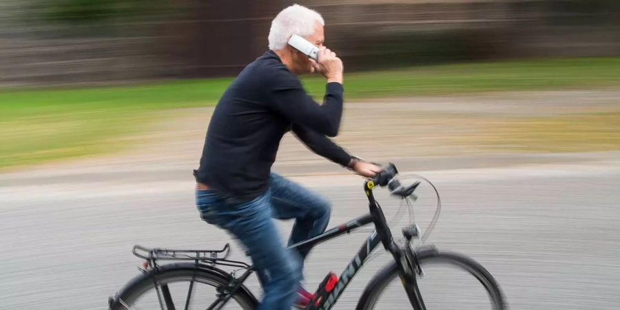 Ein Radfahrer telefoniert auf dem Velo.