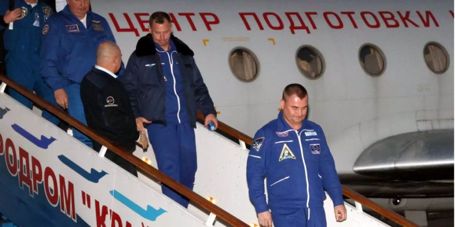 Die Raumfahrer Alexej Owtschinin (rechts) und Nick Hague (in der Mitte) steigen aus einem Flugzeug.