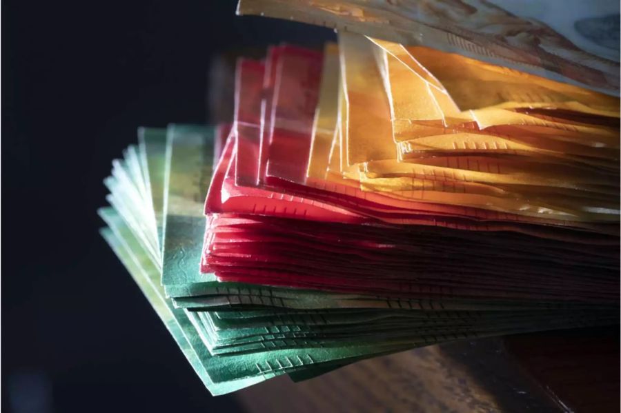 Gestapelter Haufen von 10er, 20er und 50er Banknoten halb im Schatten - Keystone