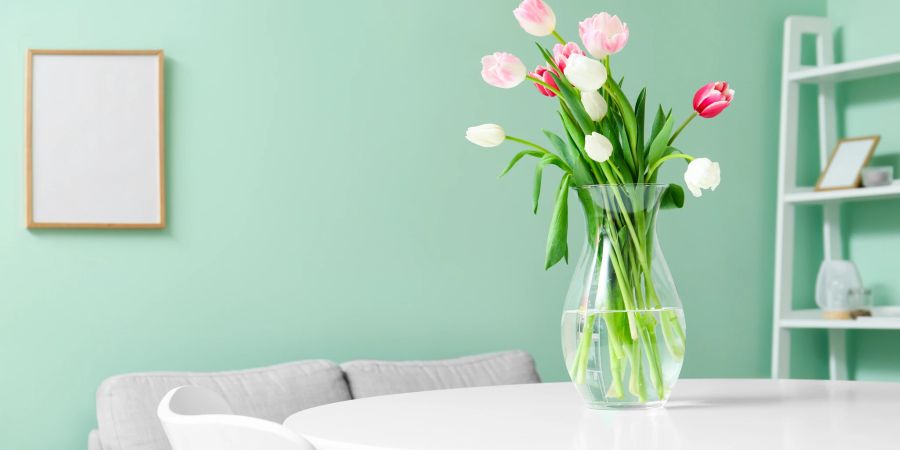 Vase mit Tulpen auf Tisch vor mintgrüner Wand