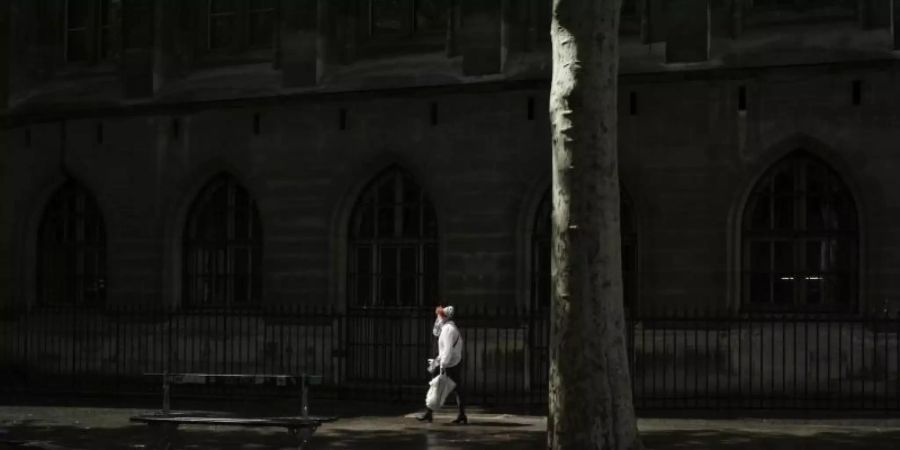 Eine Frau mit Mundschutz geht eine Strasse in Paris entlang. Foto: Thibault Camus/AP/dpa