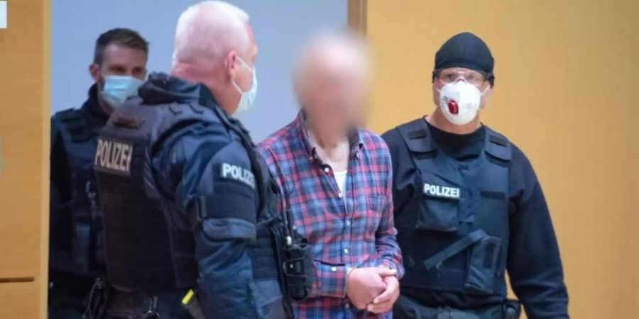 Der Angeklagte wird von einem Polizisten in den Verhandlungssaal geführt. Der Mann ist der Vater des Attentäters von Hanau. Foto: Boris Roessler/dpa