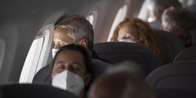 Passagiere sitzen mit Masken gegen das Coronavirus in einem Flugzeug. Coronavirus Flugzeug Passagiere