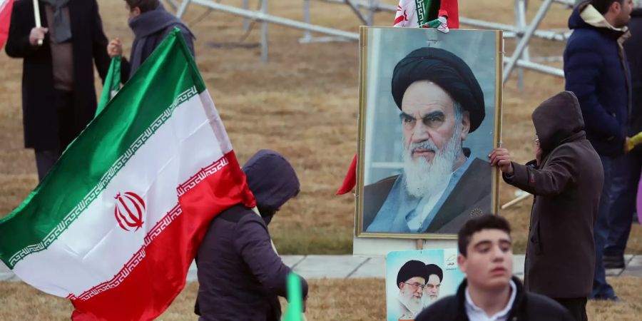 Menschen im Iran halten Flaggen und das Bild von Ayatollah Khomeini.