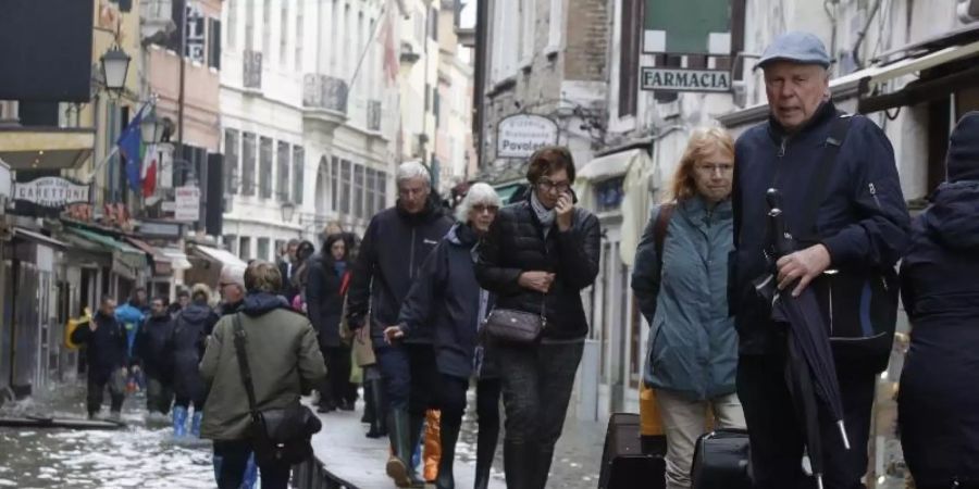 Touristen ziehen ihr Gepäck über provisorische Gehsteige. Foto: Luca Bruno/AP/dpa