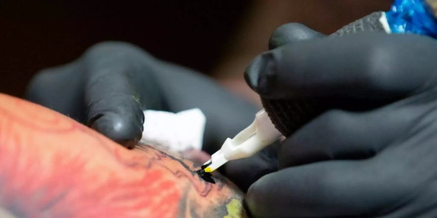 Ein Tätowierer sticht mit einer Nadel ein buntes Tattoo