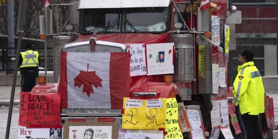 Ein Polizist in Ottawa im Gespräch mit einem Lastwagenfahrer, der sein Gefährt mit Schildern und Flaggen bedeckt hat. Foto: Adrian Wyld/The Canadian Press/AP/dpa