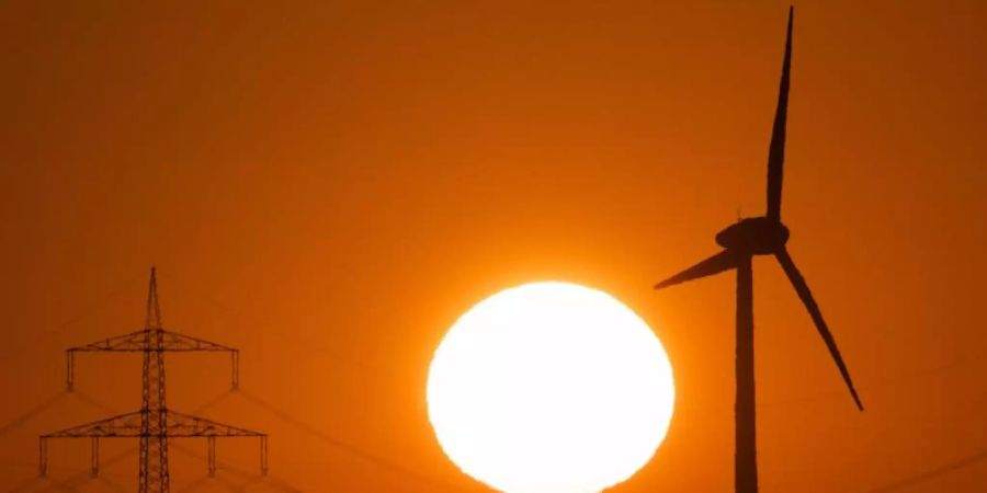 Die Silhouette eines Windrades (r) zeichnet sich vor der aufgehenden Sonne ab. Foto: Julian Stratenschulte/dpa
