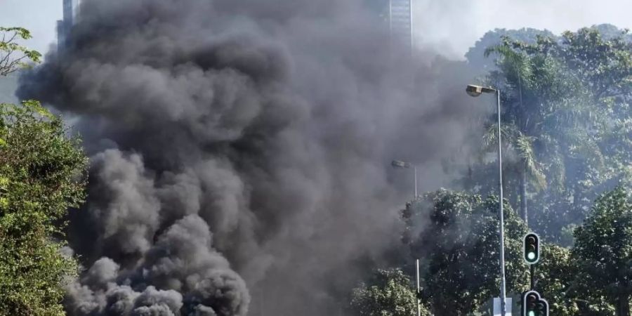 Plünderer stehen in Durban vor einem Einkaufszentrum neben einer brennenden Barrikade. Foto: Andre Swart/AP/dpa