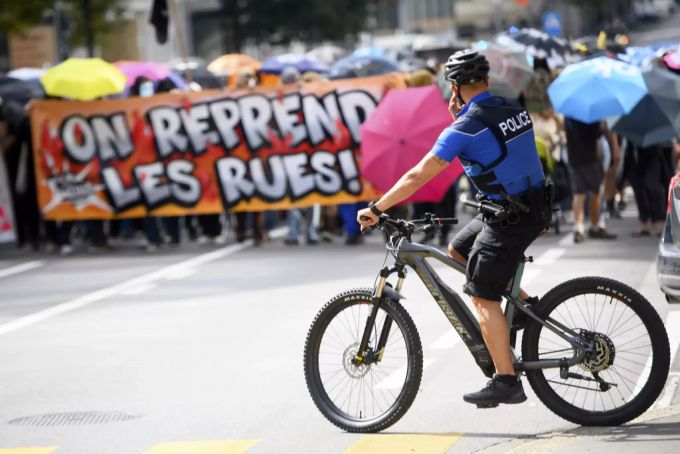 Ein Lausanner Polizist beobachtet auf einem Elektrofahrrad den Demostrantenzug. Demo Lausanne