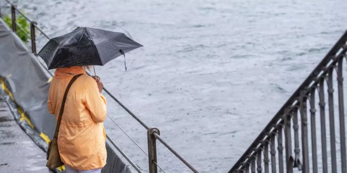 Wetter: Eine Frau beobachtet im Regen den Wasserstand in Luzern. Wetter