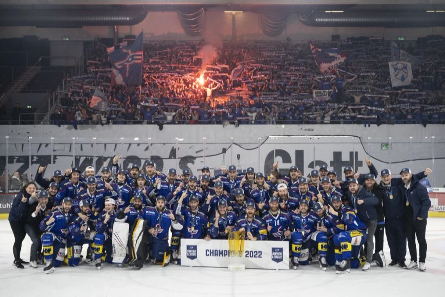 Das Team posiert auf dem Eis mit dem Pokal vor der Fan-Kurve.